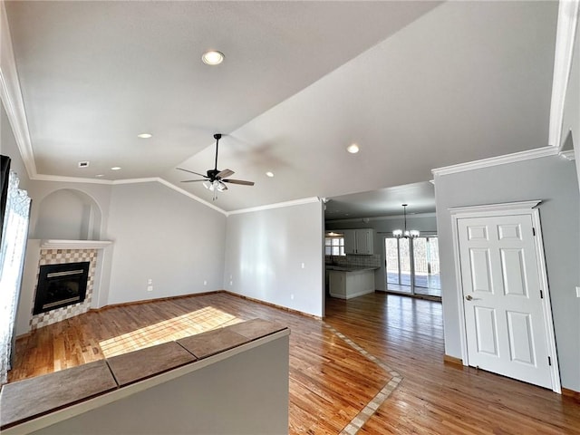 unfurnished living room featuring a stone fireplace, ceiling fan with notable chandelier, vaulted ceiling, light wood-type flooring, and crown molding