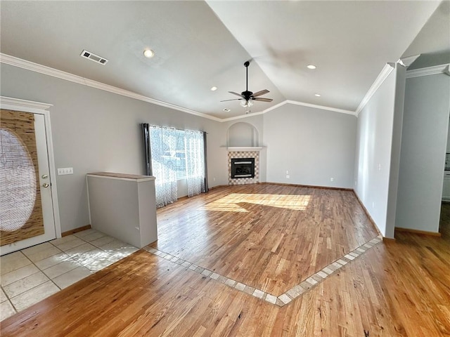 unfurnished living room with hardwood / wood-style flooring, visible vents, vaulted ceiling, ornamental molding, and a tiled fireplace