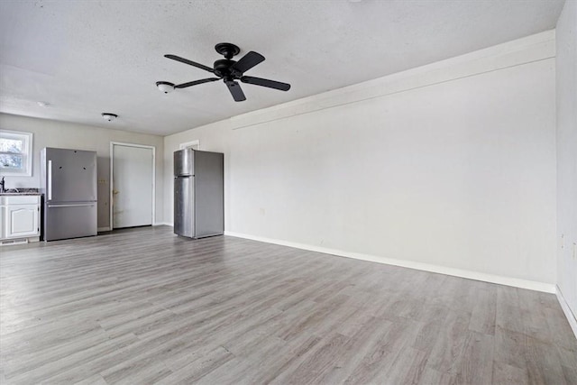 unfurnished living room with ceiling fan, light wood-type flooring, and a textured ceiling