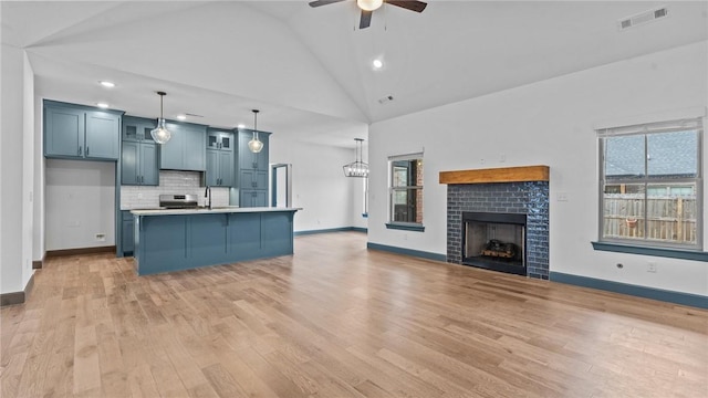 kitchen with ceiling fan, hanging light fixtures, tasteful backsplash, a tiled fireplace, and a kitchen island with sink