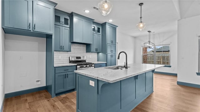 kitchen featuring pendant lighting, a kitchen island with sink, stainless steel range with gas cooktop, sink, and light stone counters