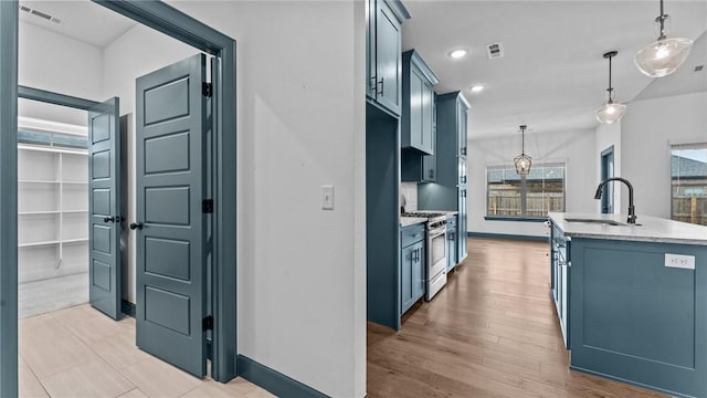 kitchen featuring sink, hanging light fixtures, stainless steel gas range oven, backsplash, and an island with sink