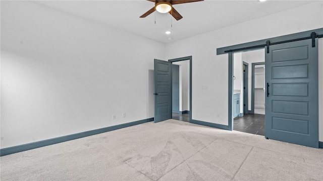 unfurnished bedroom with carpet floors, a barn door, ceiling fan, and ensuite bath