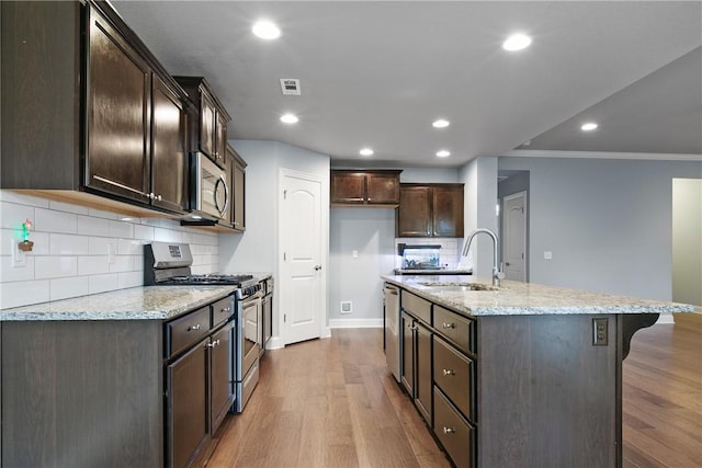 kitchen featuring hardwood / wood-style floors, sink, stainless steel appliances, light stone countertops, and a center island with sink