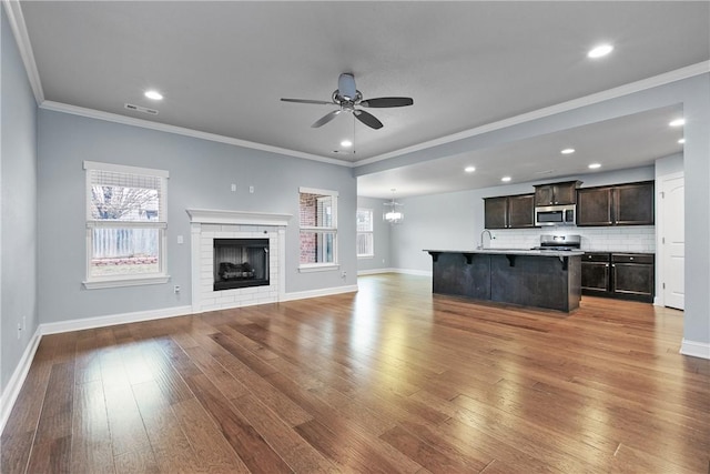 unfurnished living room featuring ceiling fan with notable chandelier, a fireplace, hardwood / wood-style floors, and crown molding