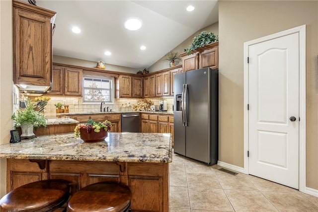 kitchen with stainless steel appliances, vaulted ceiling, light tile patterned floors, kitchen peninsula, and light stone countertops