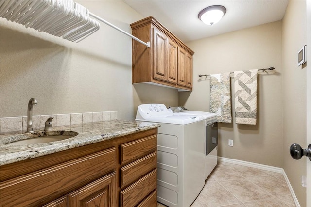 clothes washing area with sink, washer and clothes dryer, light tile patterned floors, and cabinets