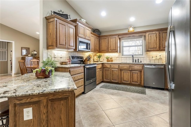 kitchen featuring lofted ceiling, sink, light stone counters, and appliances with stainless steel finishes