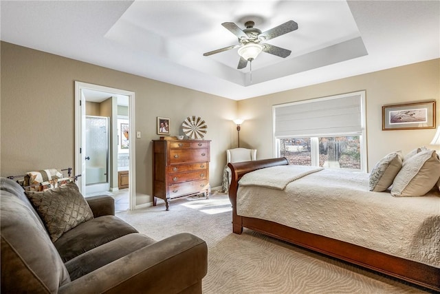 bedroom with ensuite bath, a raised ceiling, ceiling fan, and light carpet