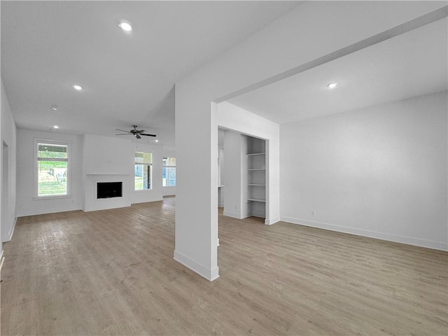 unfurnished living room featuring ceiling fan, built in features, and light wood-type flooring