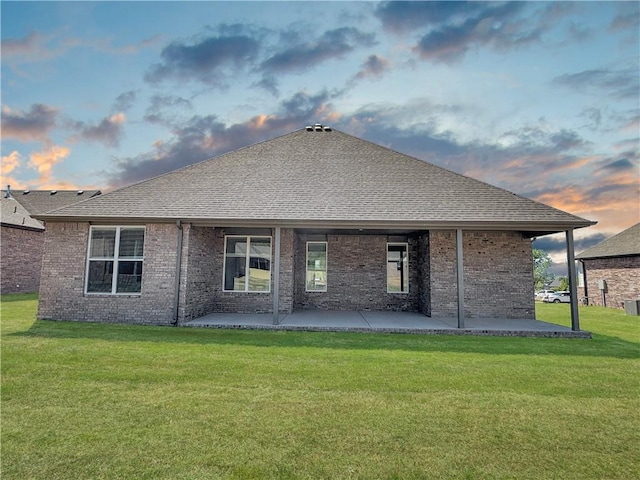 back house at dusk featuring a patio area and a lawn