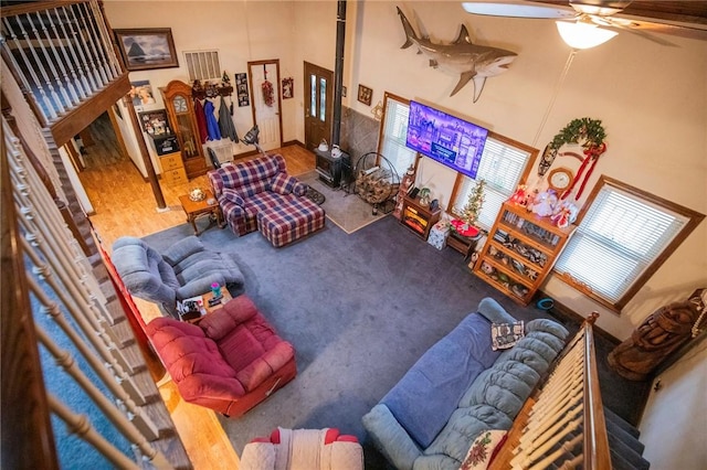 living room with a wood stove, ceiling fan, and a towering ceiling