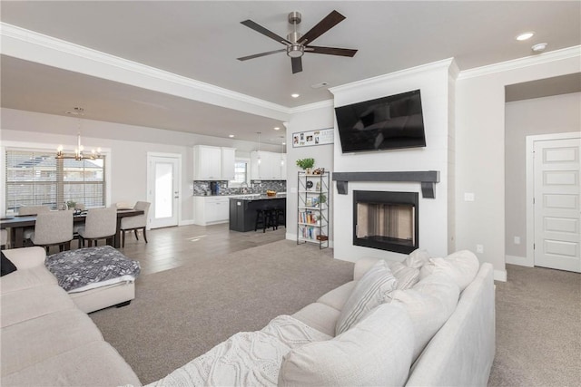 living room with ceiling fan with notable chandelier, carpet floors, and crown molding