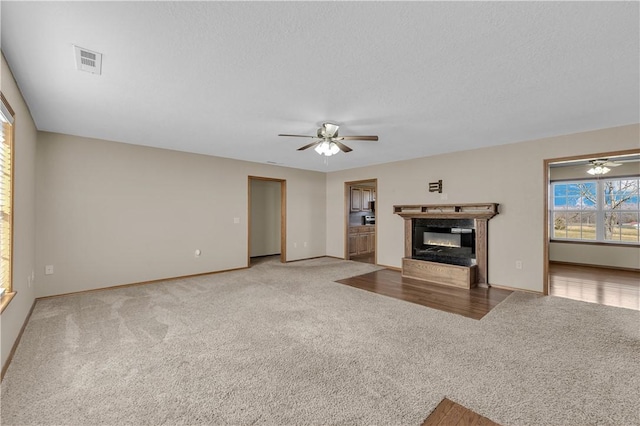 unfurnished living room featuring ceiling fan, a textured ceiling, a premium fireplace, and carpet flooring