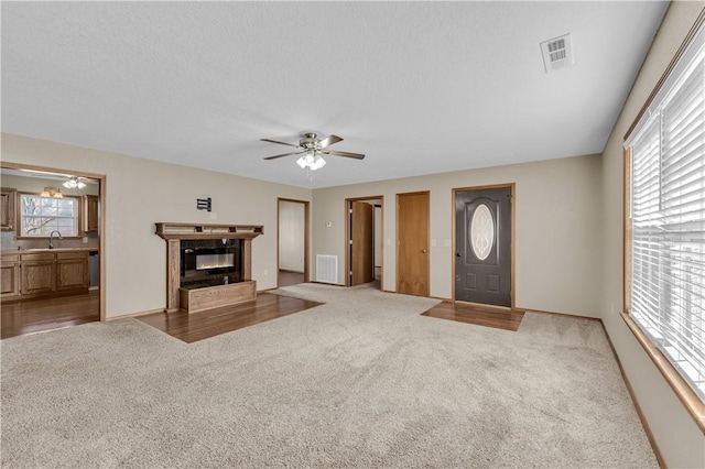 carpeted living room with ceiling fan, a high end fireplace, sink, and a textured ceiling