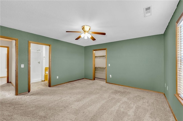 unfurnished bedroom featuring light carpet, ceiling fan, a walk in closet, and a closet