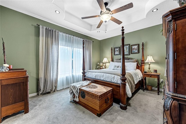 bedroom featuring light carpet, ceiling fan, a raised ceiling, and baseboards