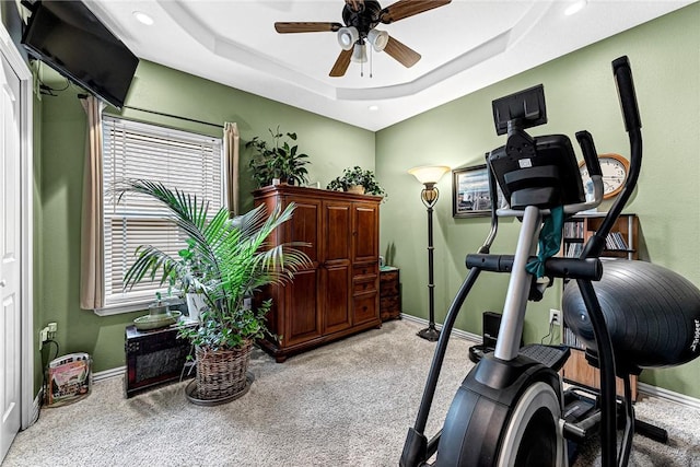 exercise room featuring baseboards, ceiling fan, a raised ceiling, and light colored carpet