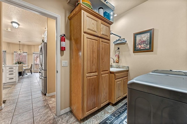 laundry area with a textured ceiling, a sink, cabinet space, and baseboards