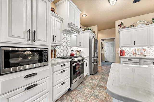 kitchen with backsplash, appliances with stainless steel finishes, white cabinetry, a textured ceiling, and light stone countertops