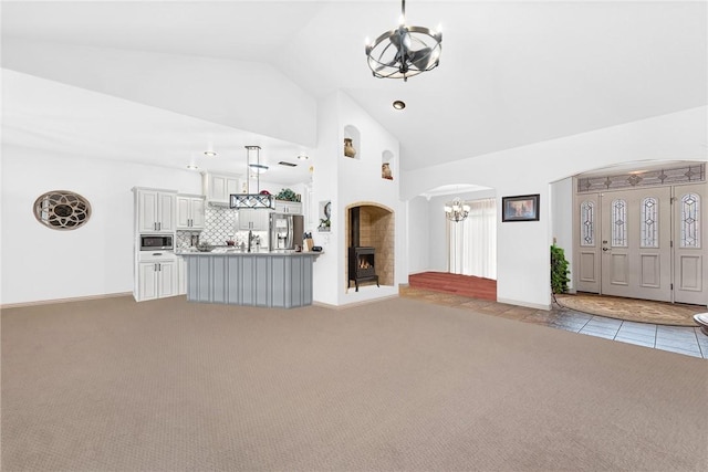 unfurnished living room with carpet, vaulted ceiling, a notable chandelier, and arched walkways