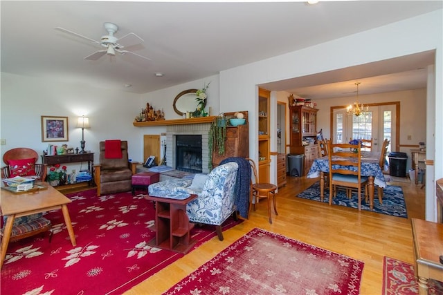 living room with hardwood / wood-style floors, ceiling fan with notable chandelier, a brick fireplace, and french doors