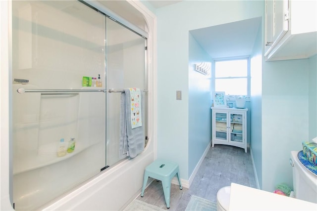 bathroom with combined bath / shower with glass door, hardwood / wood-style flooring, and toilet