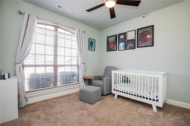 bedroom featuring ceiling fan, a crib, and light carpet