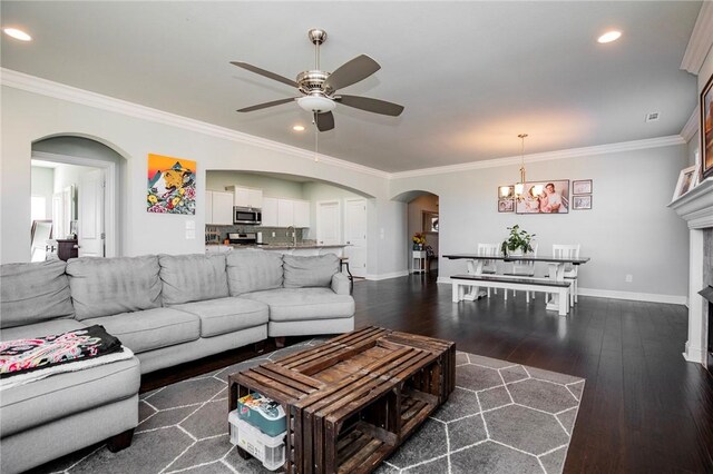 living room featuring ceiling fan with notable chandelier, dark hardwood / wood-style flooring, a tiled fireplace, and crown molding