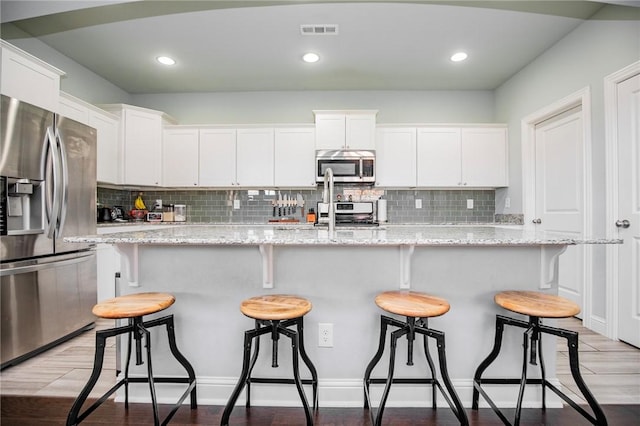 kitchen with stainless steel appliances, white cabinetry, a center island with sink, and light stone countertops