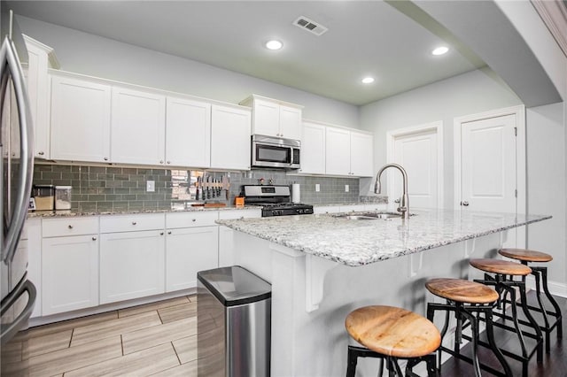 kitchen featuring white cabinets, appliances with stainless steel finishes, an island with sink, and sink