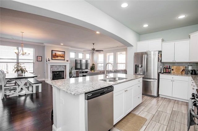 kitchen with a kitchen island with sink, stainless steel appliances, sink, white cabinetry, and ceiling fan with notable chandelier