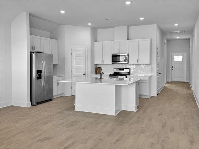 kitchen with white cabinets, appliances with stainless steel finishes, a center island with sink, and tasteful backsplash