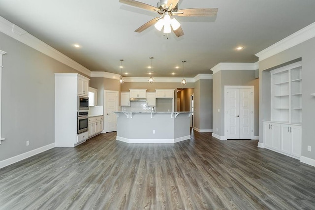 kitchen with pendant lighting, a kitchen island with sink, built in shelves, built in microwave, and white cabinetry