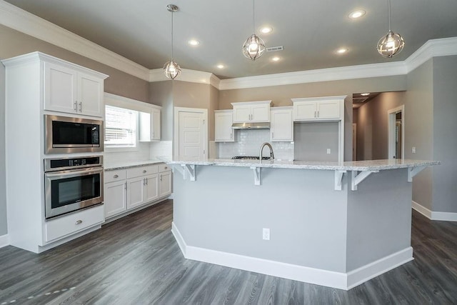 kitchen with hanging light fixtures, a center island with sink, white cabinets, and stainless steel appliances