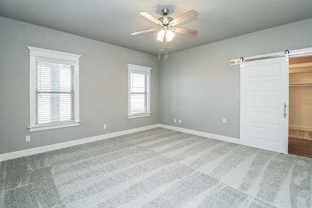 unfurnished bedroom featuring carpet flooring, a barn door, multiple windows, and ceiling fan