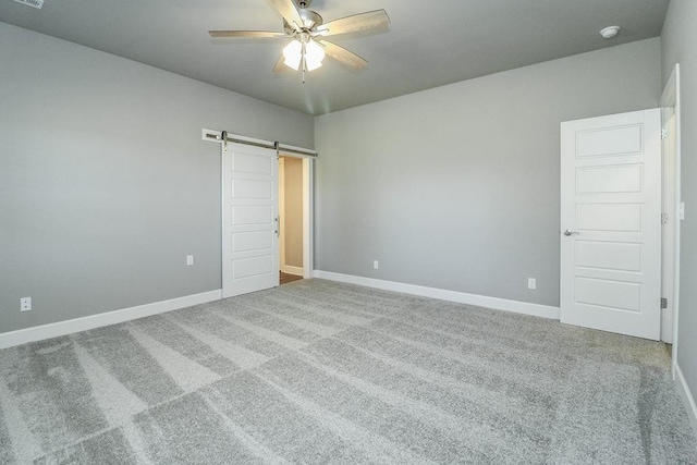 unfurnished bedroom with a barn door, ceiling fan, and carpet