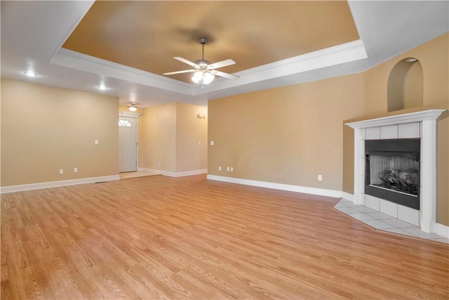 unfurnished living room featuring a tray ceiling, a tile fireplace, baseboards, light wood-style floors, and ceiling fan