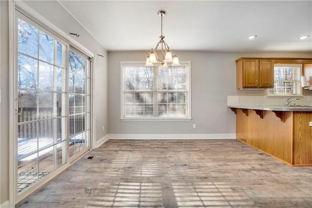 unfurnished dining area featuring an inviting chandelier, a sink, baseboards, and light wood-type flooring