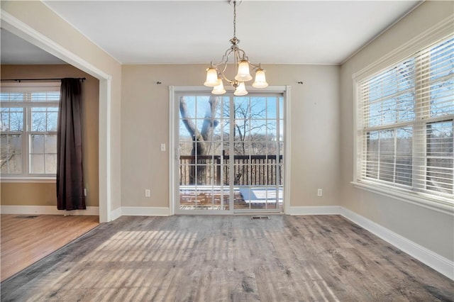 unfurnished dining area featuring plenty of natural light, baseboards, wood finished floors, and a chandelier