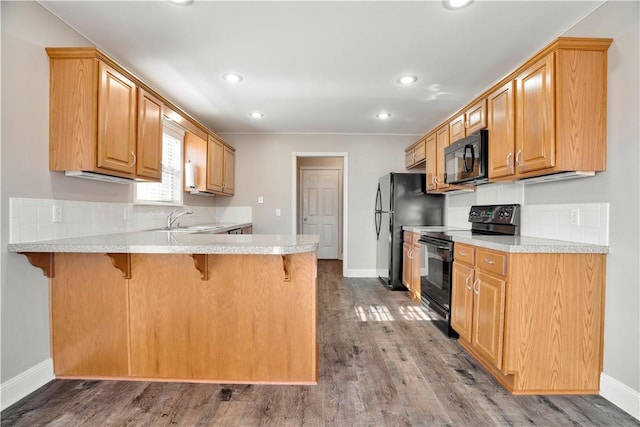 kitchen featuring a peninsula, a breakfast bar, dark wood-type flooring, a sink, and black appliances
