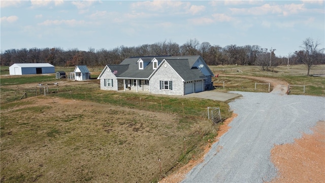 view of front of house featuring a garage, gravel driveway, a rural view, and an outdoor structure