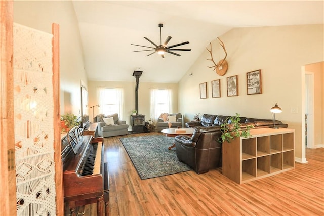 living room with ceiling fan, wood-type flooring, a wood stove, and vaulted ceiling