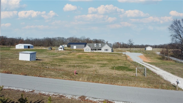 view of yard featuring a shed, a detached garage, an outbuilding, and a rural view