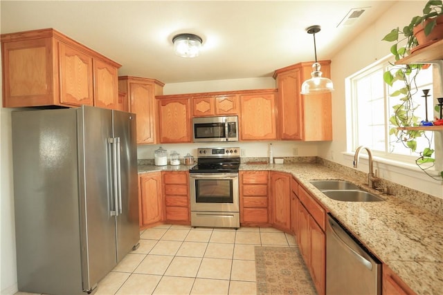 kitchen featuring appliances with stainless steel finishes, light stone counters, sink, light tile patterned floors, and hanging light fixtures