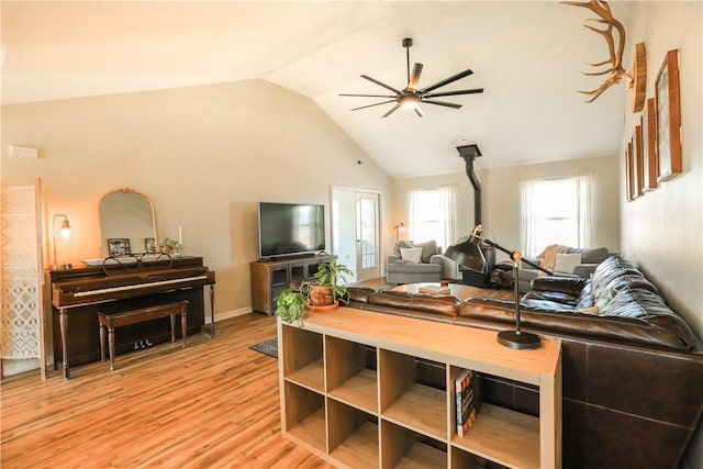 living area with high vaulted ceiling, a wood stove, ceiling fan, and light wood-style flooring