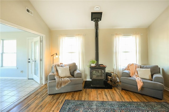 sitting room featuring lofted ceiling, visible vents, a wood stove, wood finished floors, and baseboards