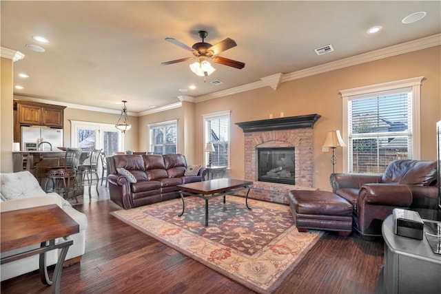 living room featuring a brick fireplace, ceiling fan, dark wood-type flooring, and ornamental molding