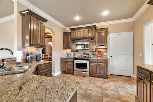 kitchen with stainless steel appliances, light stone counters, crown molding, and sink