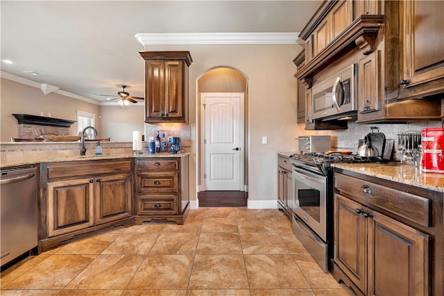 kitchen featuring crown molding, ceiling fan, appliances with stainless steel finishes, tasteful backsplash, and light stone counters